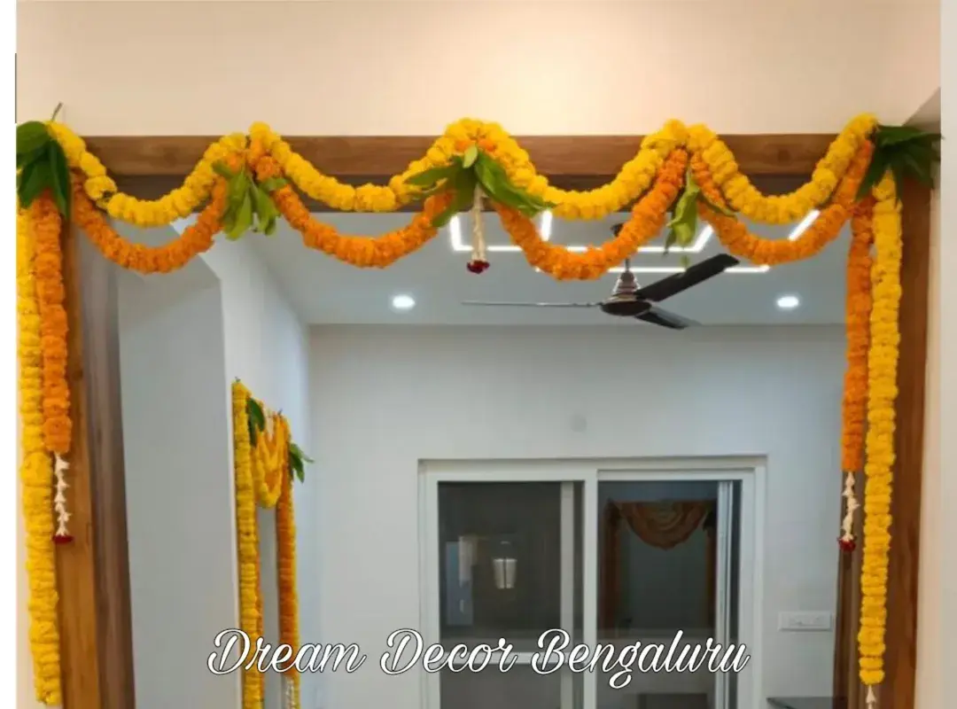 An inside doorway in a new flat framed with yellow and orange marigold strings and mango leaves, with more marigold on a second doorway behind