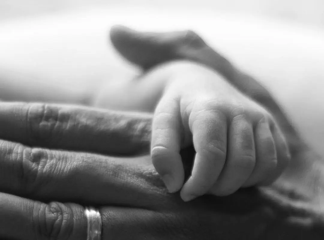 Black and white close-up of a newborn's hand resting on an adult's open palm, no faces