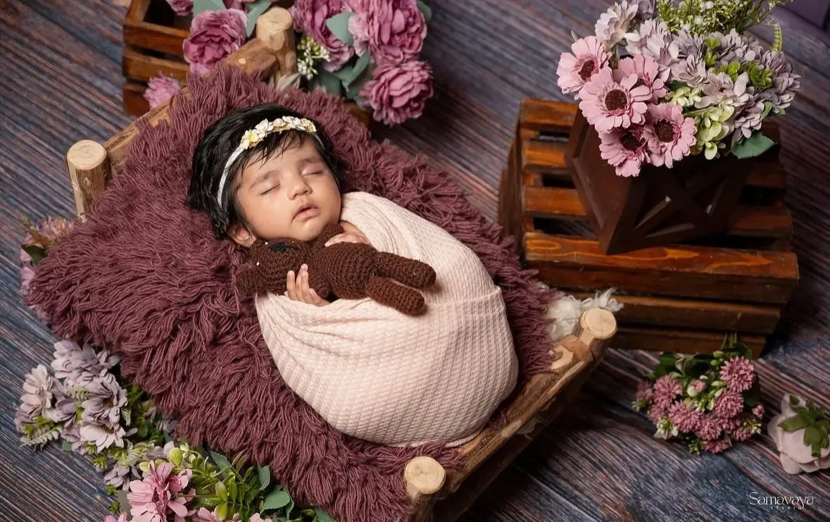 A built studio set: a miniature wooden bed with a crochet teddy and two crates of flowers around the baby