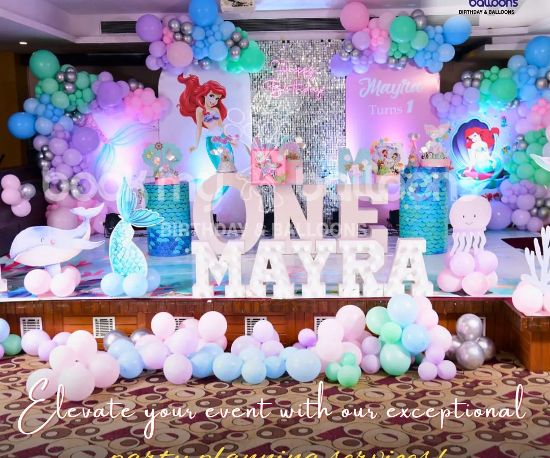 For Mayra's first birthday, we created an underwater mermaid kingdom. This elaborate stage setup includes character cutouts of Ariel, balloon sculptures of a whale and octopus, and a shimmering backdrop, all tied together with a sea of pastel and chrome balloons.