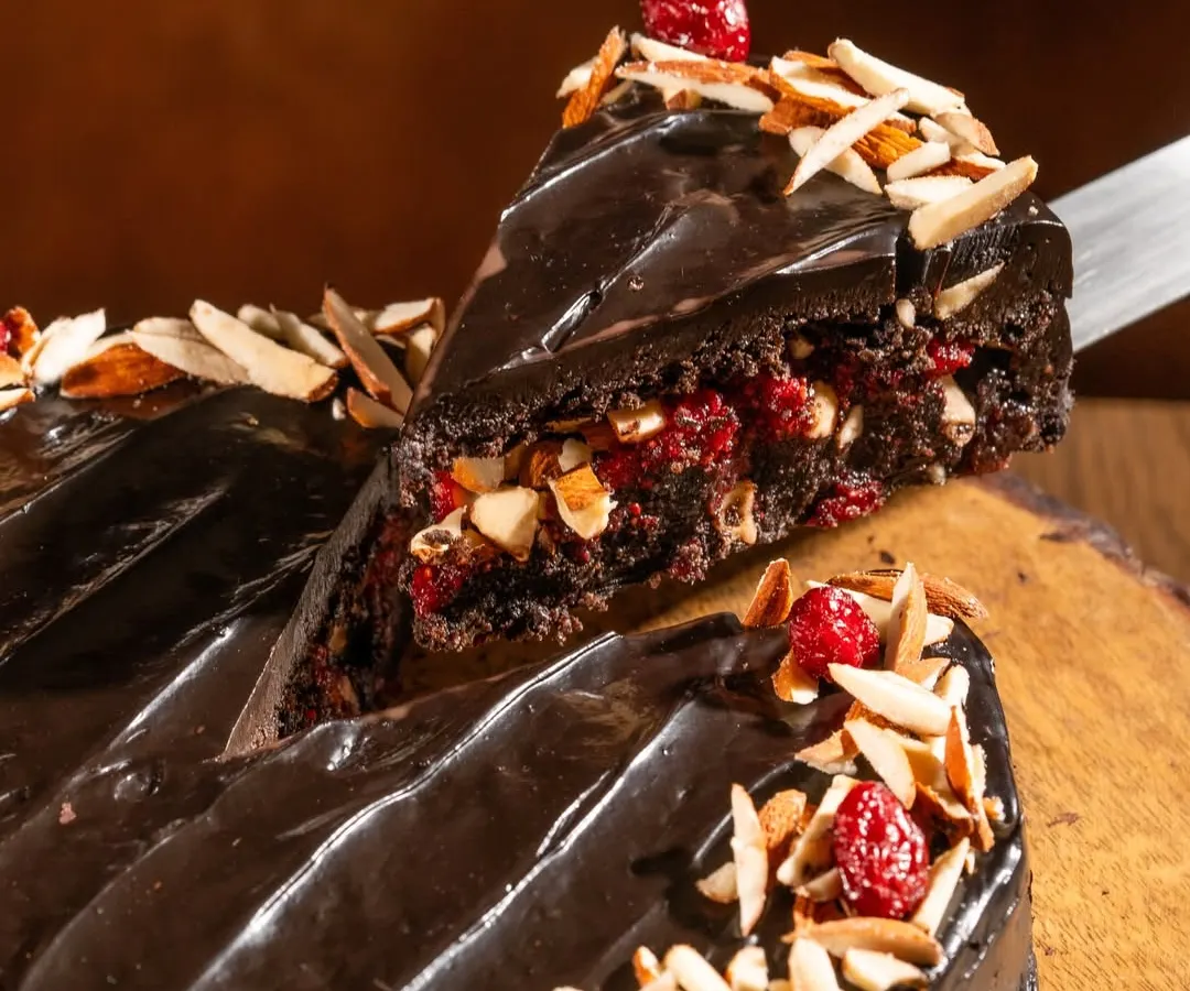 Here’s a close look at our star creation. You can see the rich, dense texture of the oat flour sponge, the bright pop of our house-made cranberry compote, and the generous topping of toasted almonds. The glossy finish comes from a silky vegan chocolate ganache we make with coconut milk.