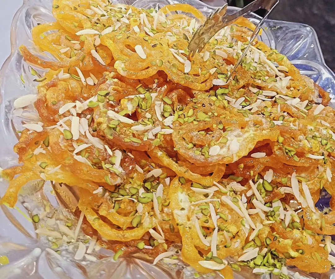Nothing beats a classic Indian dessert. This is my freshly made jalebi, garnished with slivered almonds and pistachios, served in a beautiful glass dish. It's a sweet and crispy favorite at many social gatherings.