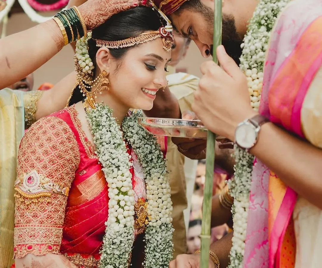 A beautiful moment from a traditional South Indian wedding. I designed this bride's classic red Kanchivaram saree blouse with intricate, heavy embroidery covering the sleeves for a regal muhurtham look.