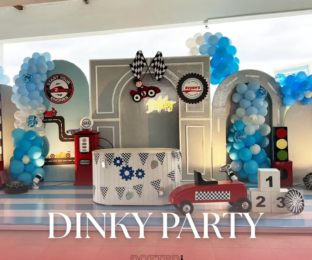 For a little one who loves cars, I created this 'Dinky Party' theme. The setup features a custom backdrop with a gas station, traffic lights, and checkered flag details, all framed by blue and white balloon garlands to get the engines started.