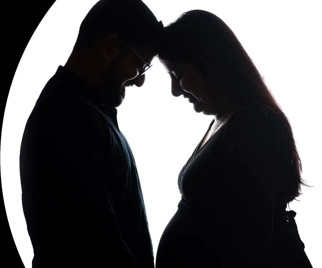 An intimate silhouette portrait of an expecting couple, their foreheads touching in a moment of quiet connection. This artistic maternity photo uses backlighting to create a beautiful, high-contrast image that focuses on their bond and the shape of the baby bump.