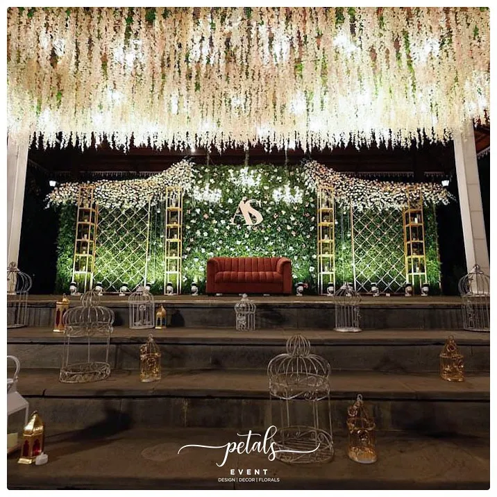 For receptions, I love designing spaces that feel both glamorous and inviting. This stage features a lush green fern wall dotted with flowers, a cascading floral ceiling, and a comfortable velvet sofa, creating a luxurious yet relaxed setting for the couple to celebrate.