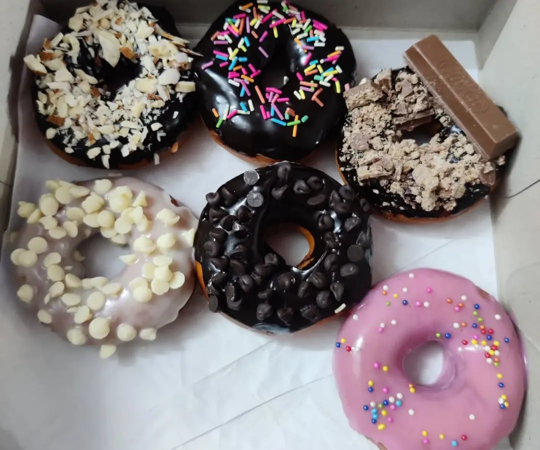 A box of my assorted homemade donuts. This one includes toppings like white and dark chocolate chips, crushed KitKat, slivered almonds, rainbow sprinkles, and a simple strawberry glaze.