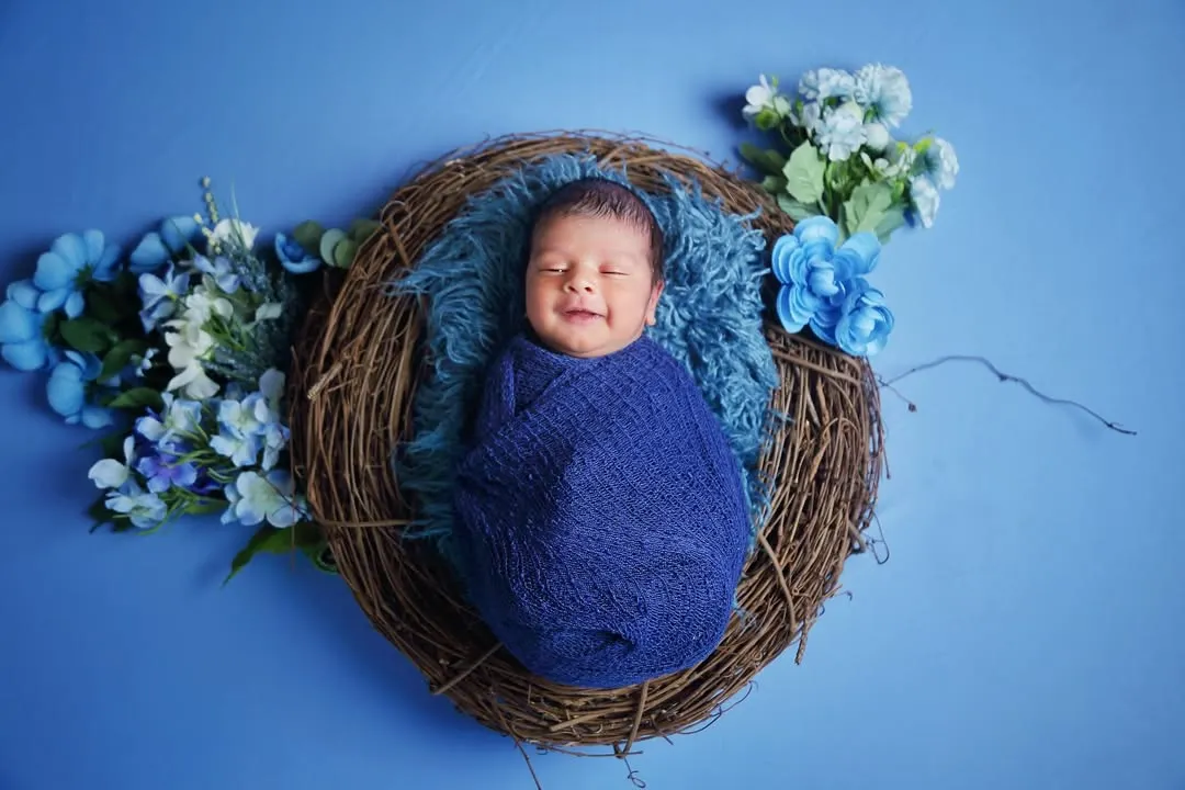 Capturing that perfect, sleepy newborn smile is my specialty. For this shot, I used a cozy nest prop with a vibrant blue theme, complete with floral accents, to create a peaceful and visually striking portrait.