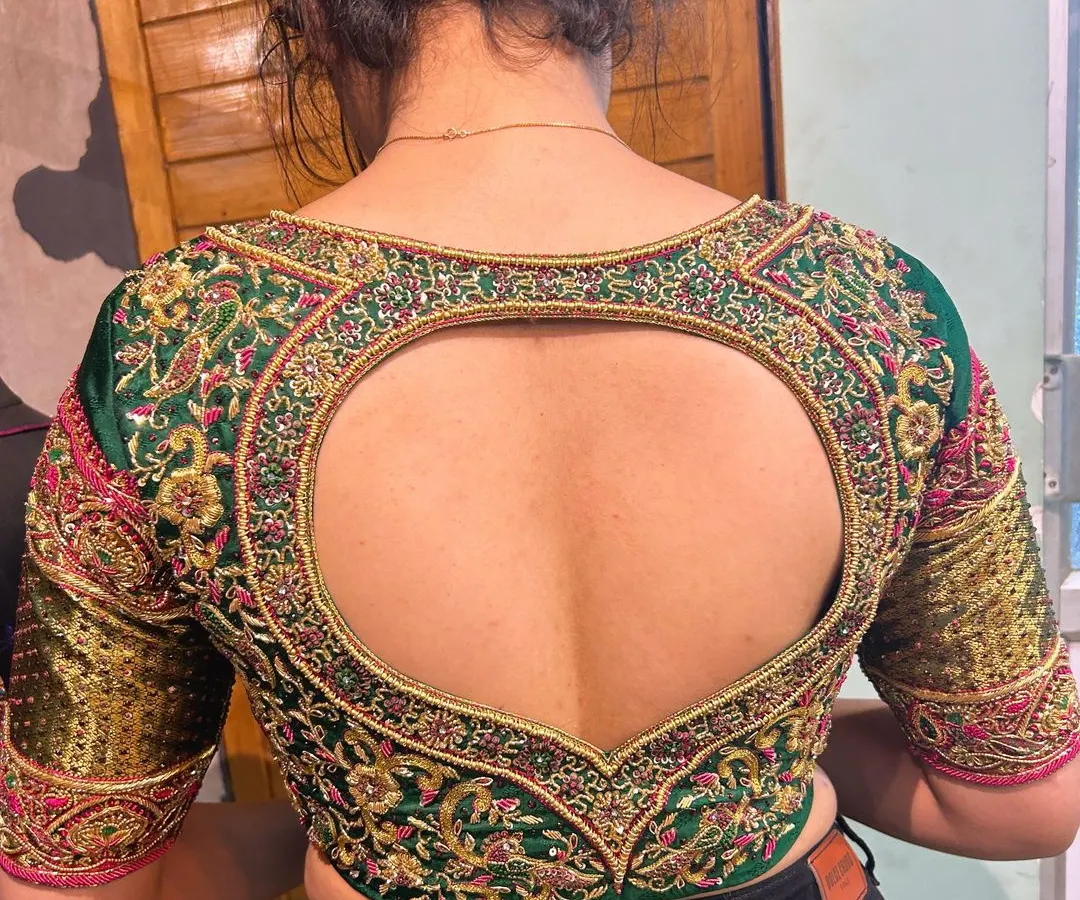 A perfect example of how a blouse can be a statement piece. This emerald green bridal blouse features a dramatic heart-shaped cutout, framed with dense zardosi and resham embroidery. The sleeves are equally detailed, making it stunning from every angle.