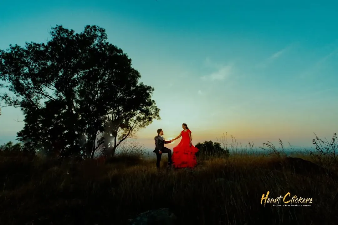 A breathtaking sunset silhouette on a hilltop. The bride's vibrant red gown flows dramatically against the twilight sky, creating a truly epic and romantic pre-wedding portrait.