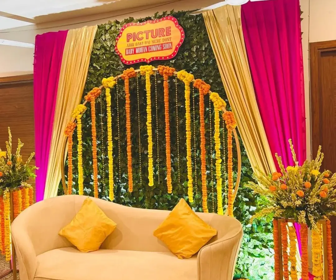 For a traditional Godh Bharai with a twist, we designed this vibrant 'Filmy' theme. The combination of a lush green wall, bright marigold garlands, and dramatic draping creates a festive and uniquely Indian celebration space.