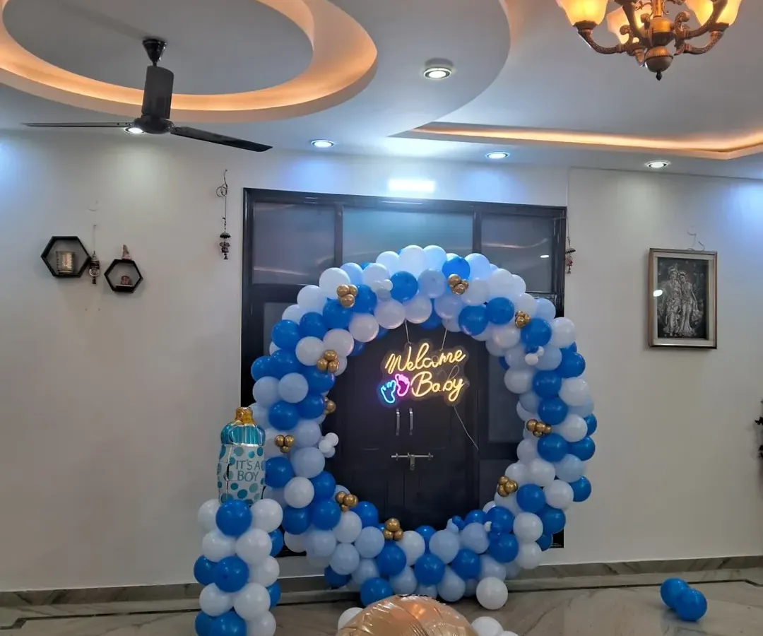 This is a classic "Welcome Boy" decoration featuring a full ring balloon arch in blue, white, and gold. The bright "Welcome Boy" neon sign makes it a perfect photo backdrop for your celebration at home.