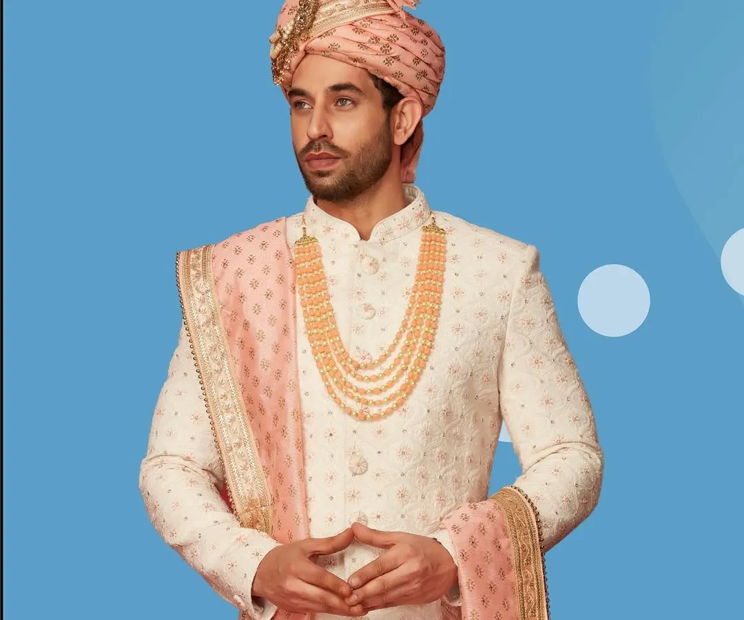 We believe every groom deserves to feel like royalty. This classic ivory sherwani with intricate embroidery, paired with a pastel pink safa and dupatta, is a timeless choice for a regal wedding look.