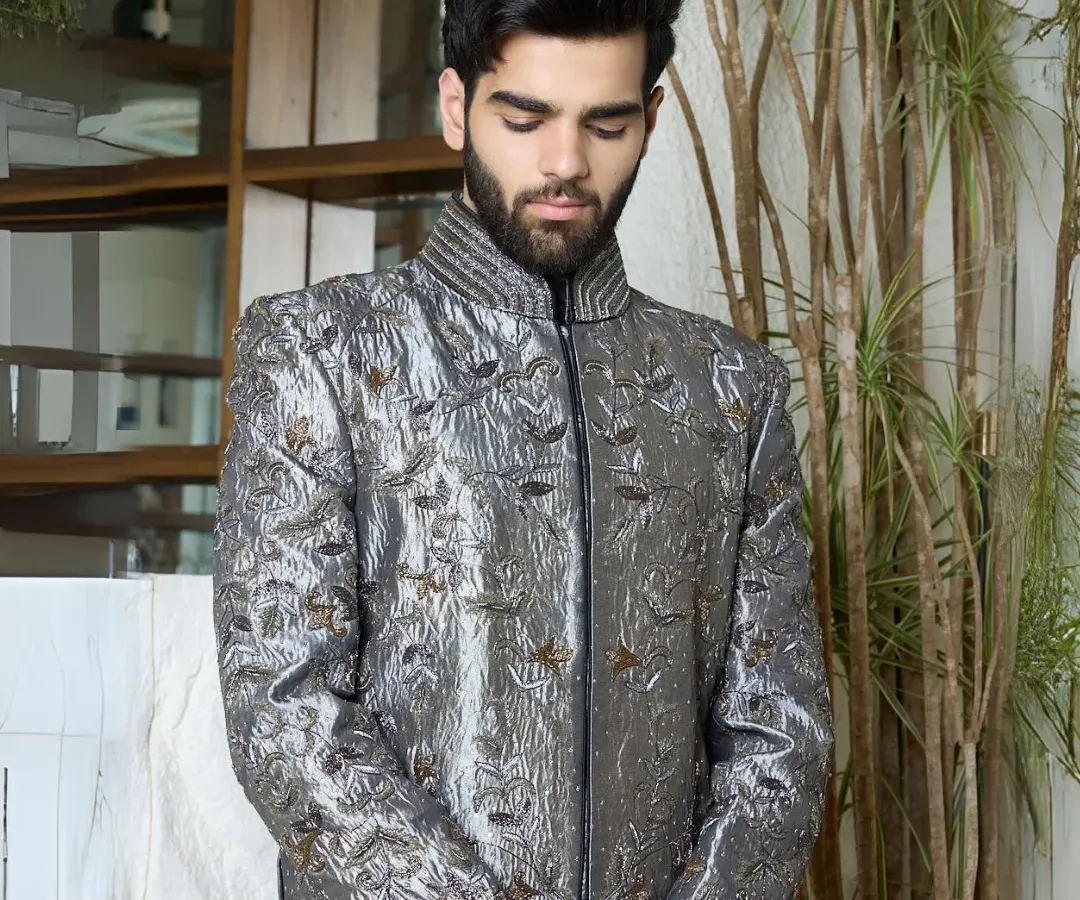 A masterpiece in gunmetal silk, this sherwani is elevated with intricate all-over threadwork. The sculpted shoulders and textural cuffs create a powerful blend of regality and modern edge, perfect for a groom or for making a statement at a grand event.