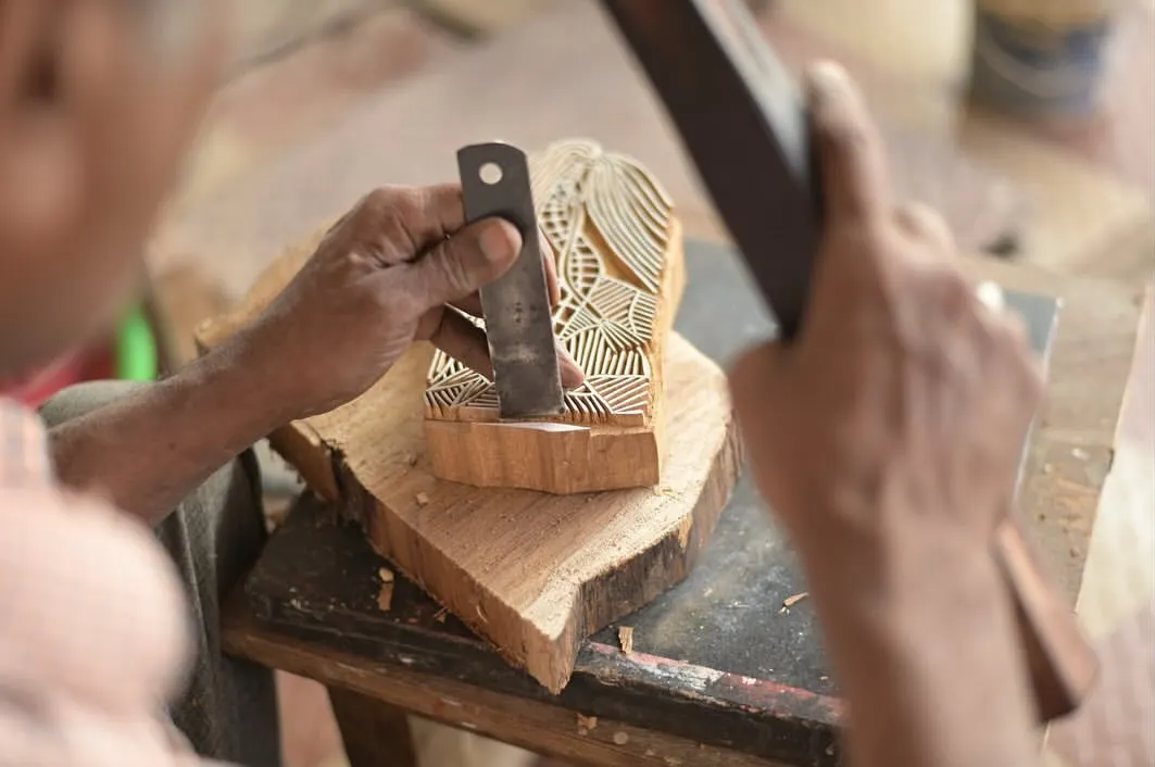The heart of our craft lies in the hands of our master carvers. Here, an artisan chisels away at a piece of teak wood, bringing an intricate design to life. This level of detail and skill is what makes each print a unique piece of art.