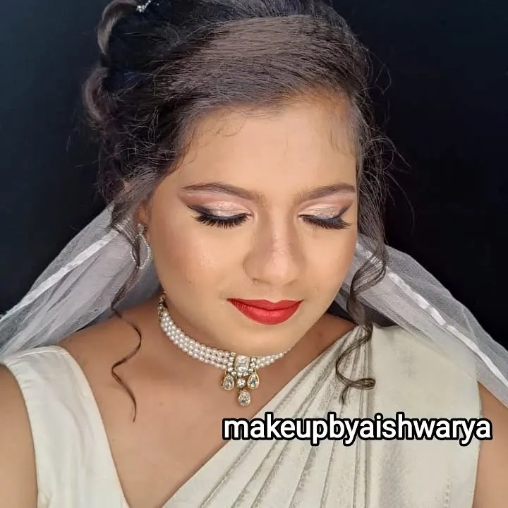 This is an elegant Christian bridal look I created for a white saree ceremony. The makeup is soft and glowing, with shimmery champagne eyeshadow, winged liner, and a classic red lip, complemented by a delicate pearl necklace.