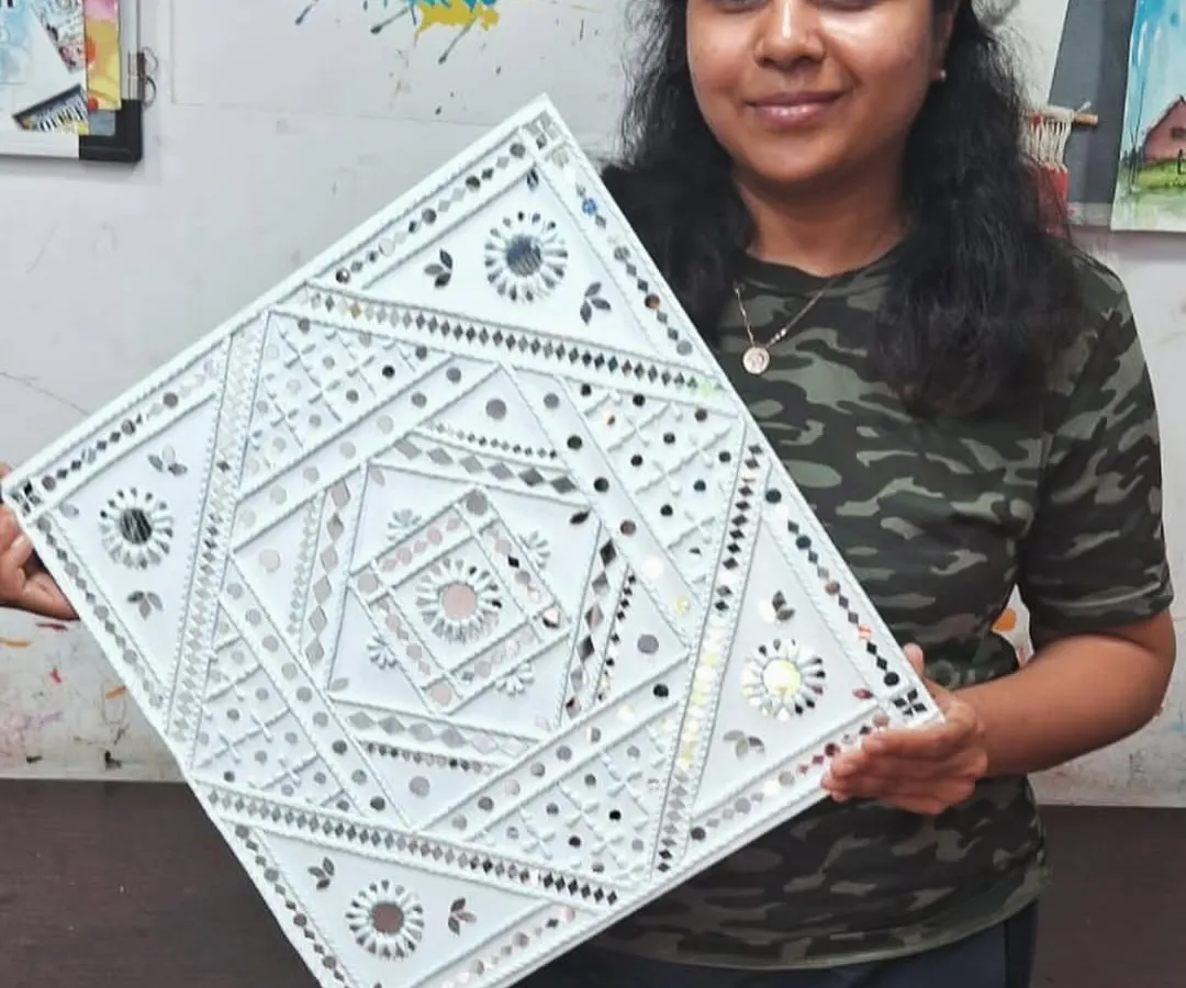 The proud smile of a student holding her completed Lippan art piece. In our classes, you will learn to create these beautiful, traditional mud and mirror designs to decorate your home.