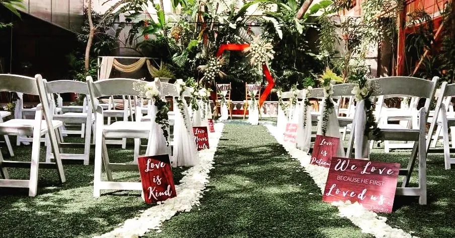 We create elegant and memorable pathways for your most special moments. This Christian wedding aisle is lined with fresh white rose petals and personalized signs, leading to a beautifully decorated altar in a lush garden setting.