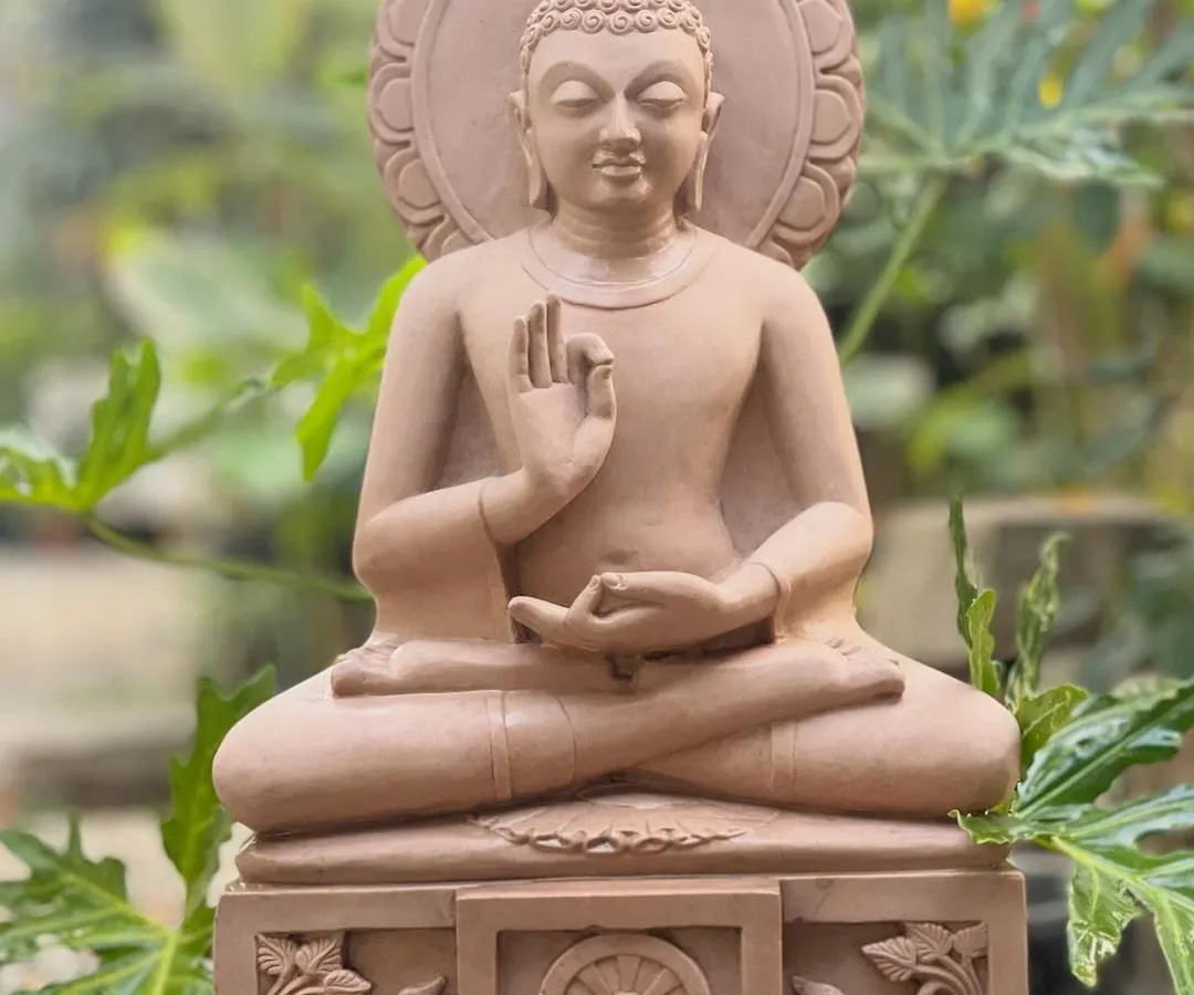 This serene Gautama Buddha statue, hand-carved from pink sandstone, is shown in the dharmachakra pravartana mudrā, or the teaching posture. It is a perfect sculpture for creating a peaceful atmosphere in any indoor or garden space.