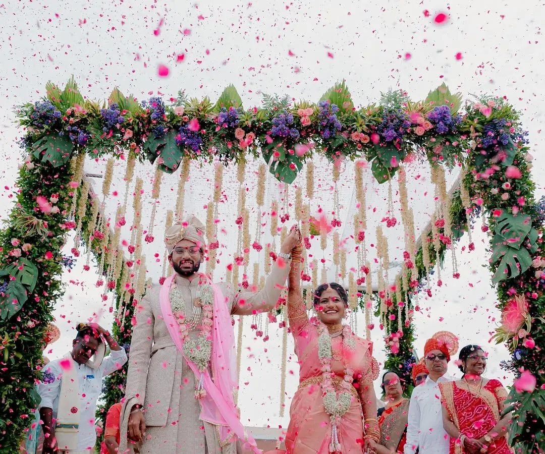 A moment of pure celebration as the happy couple is showered in flower petals under a stunning floral mandap. This is the kind of joyful, vibrant memory I love to capture, freezing the peak of happiness in time.