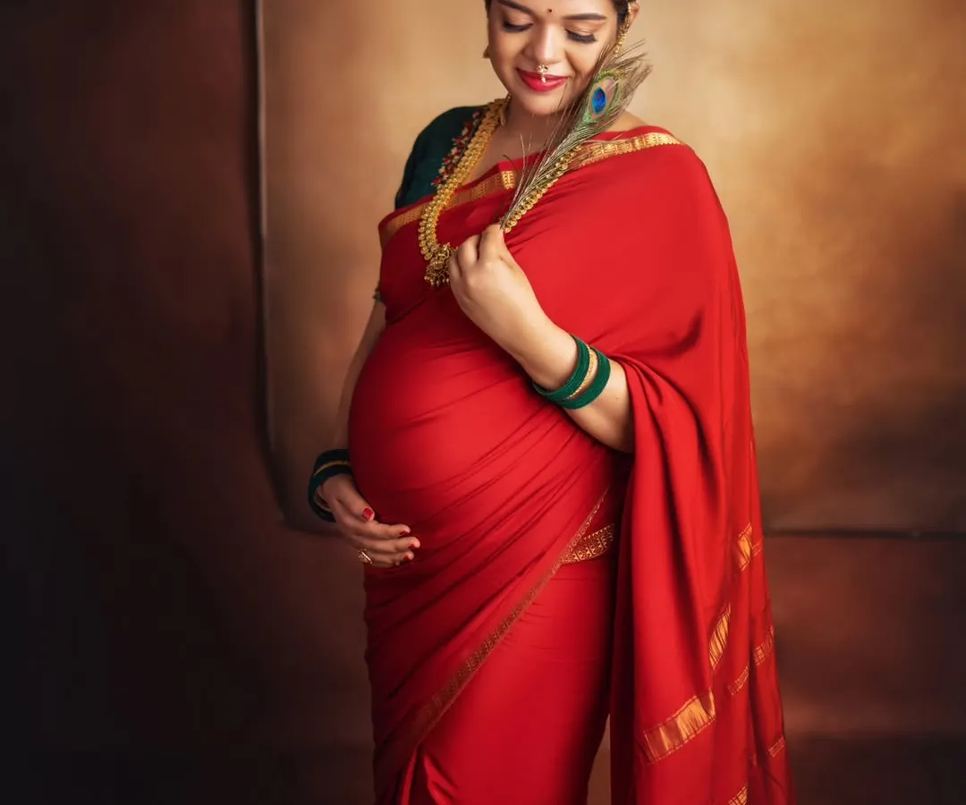 There is a unique power and grace in a traditional maternity portrait. This mom-to-be looks absolutely regal in a classic red silk saree, adorned with temple jewelry and a peacock feather, celebrating her journey with timeless elegance.
