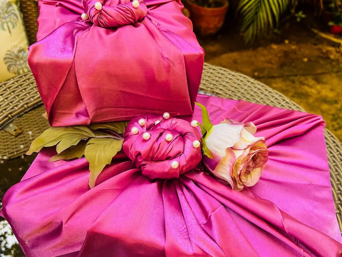 My luxury trousseau packing service transforms your gifts into works of art. Here, presents are wrapped in regal magenta satin fabric, finished with intricate pearl detailing and a delicate rose accent, ensuring the presentation is as memorable as the gift inside.