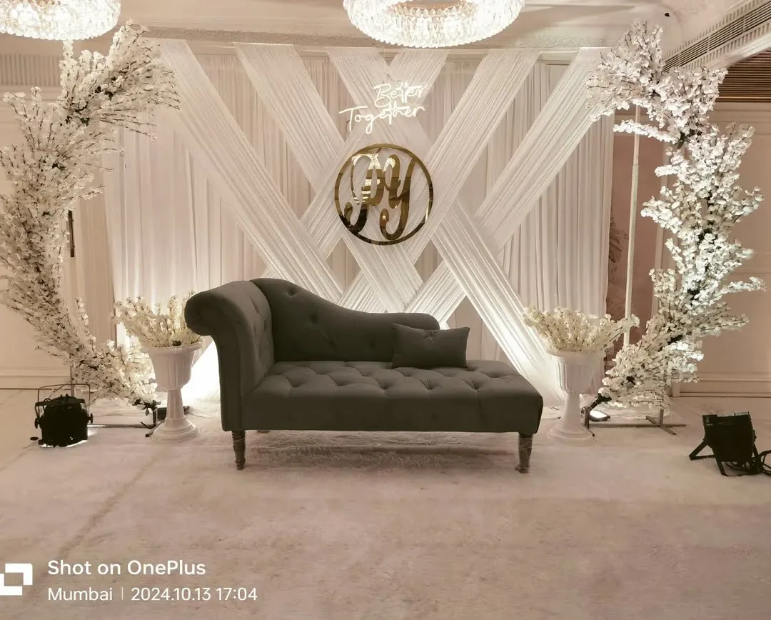 For a sophisticated engagement, we designed this all-white theme with crisscross draping, cherry blossom trees, and a custom neon sign. The elegant chaise lounge completes this clean, modern look for a banquet hall.