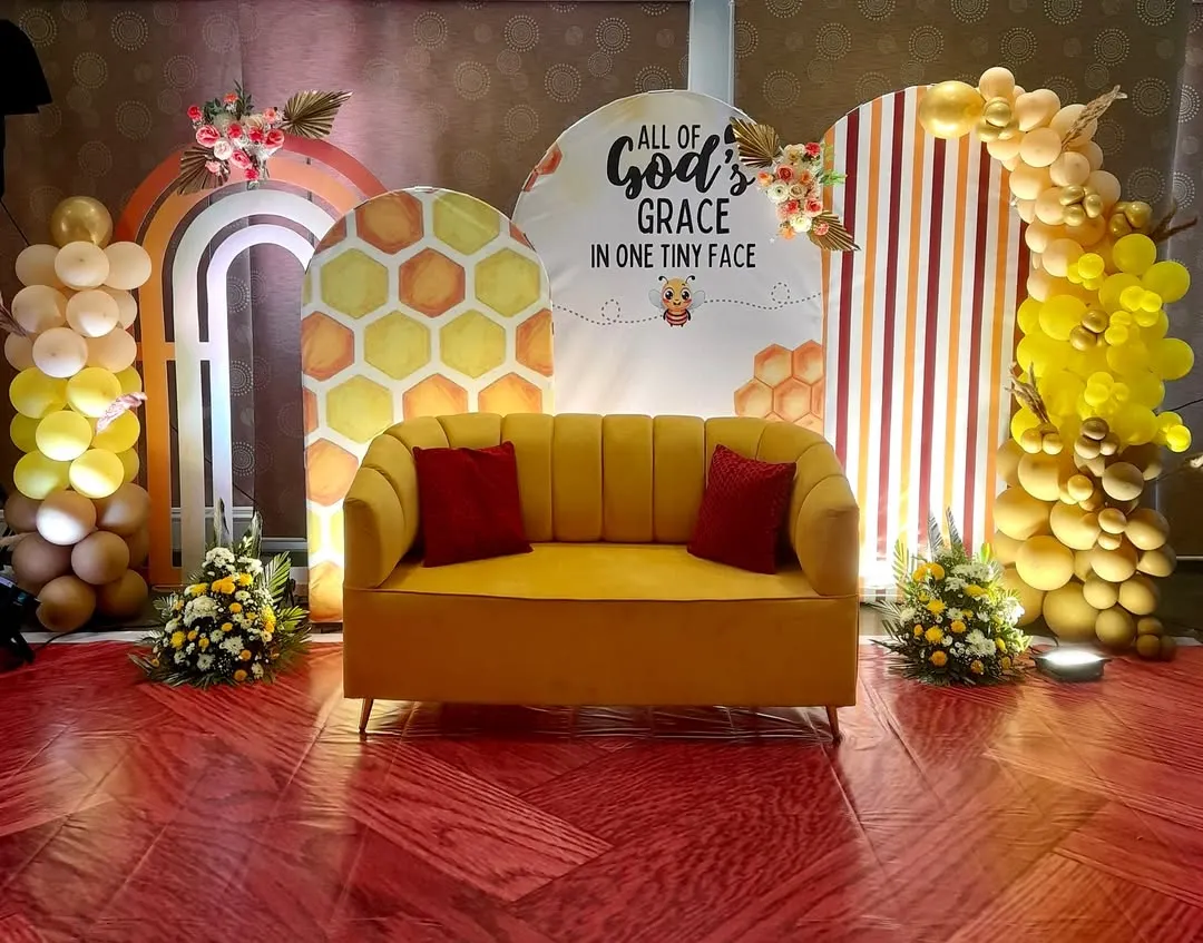 This cheerful and modern baby shower setup uses a 'sweet as can bee' honeycomb theme. We designed custom arched backdrops with warm stripes and honeycomb patterns, complemented by a vibrant yellow balloon arch and a comfortable sofa for the parents-to-be.