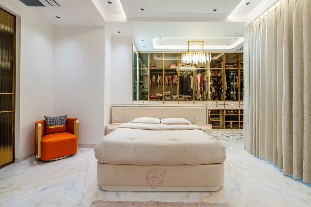 This master bedroom is a sanctuary of tranquility and style. We designed it around an open, walk-in closet with glass and gold-trimmed doors, creating a stunning focal point. The space is a testament to our belief that a bedroom should be both a personal retreat and a masterpiece of design.