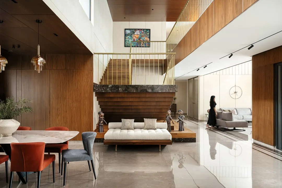 Inside Villa Shakthi in Kerala, a double-height volume connects the dining and family areas. The staircase is a sculptural element, transitioning from marble to wood and steel, creating a dramatic focal point that anchors the home's social core. This view highlights our integrated approach to interior architecture and material expression.