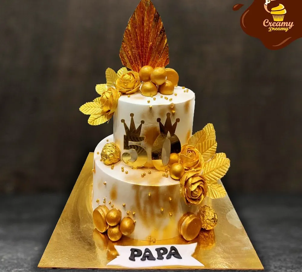 A grand celebration for a grand man. This two-tier golden jubilee cake was designed for a 50th birthday, featuring elegant gold accents, crowns, and a "Papa" banner to honor the special milestone.