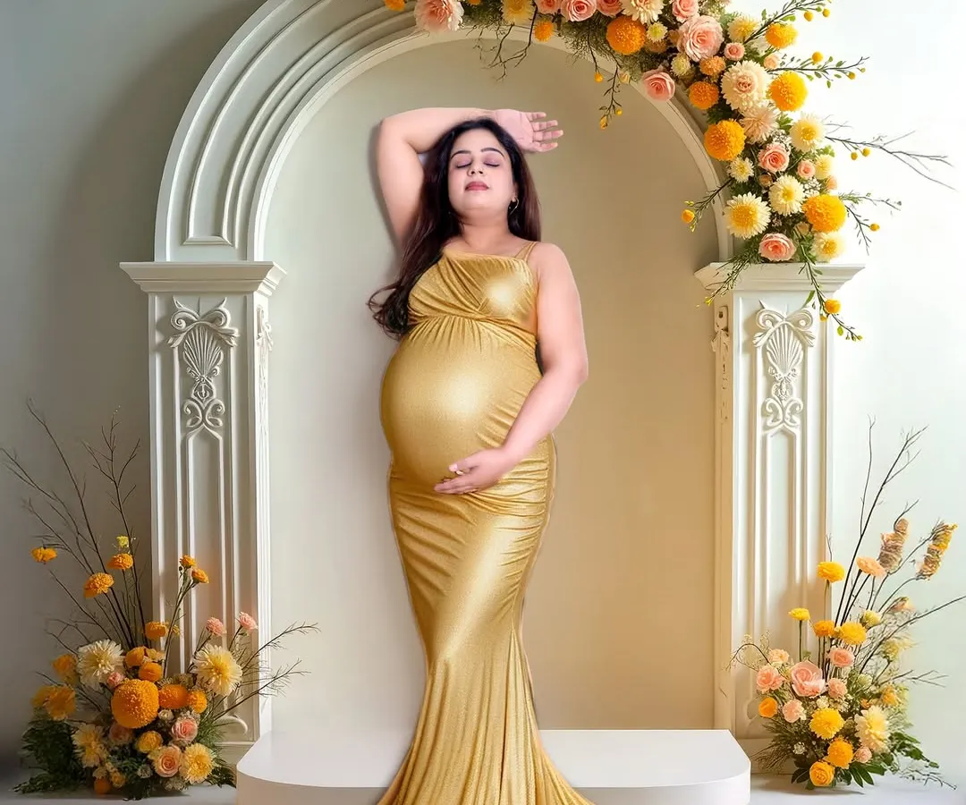 A glamorous solo maternity portrait featuring a stunning mom-to-be in a golden gown. The elegant floral arch and studio lighting highlight the beauty and glow of pregnancy.