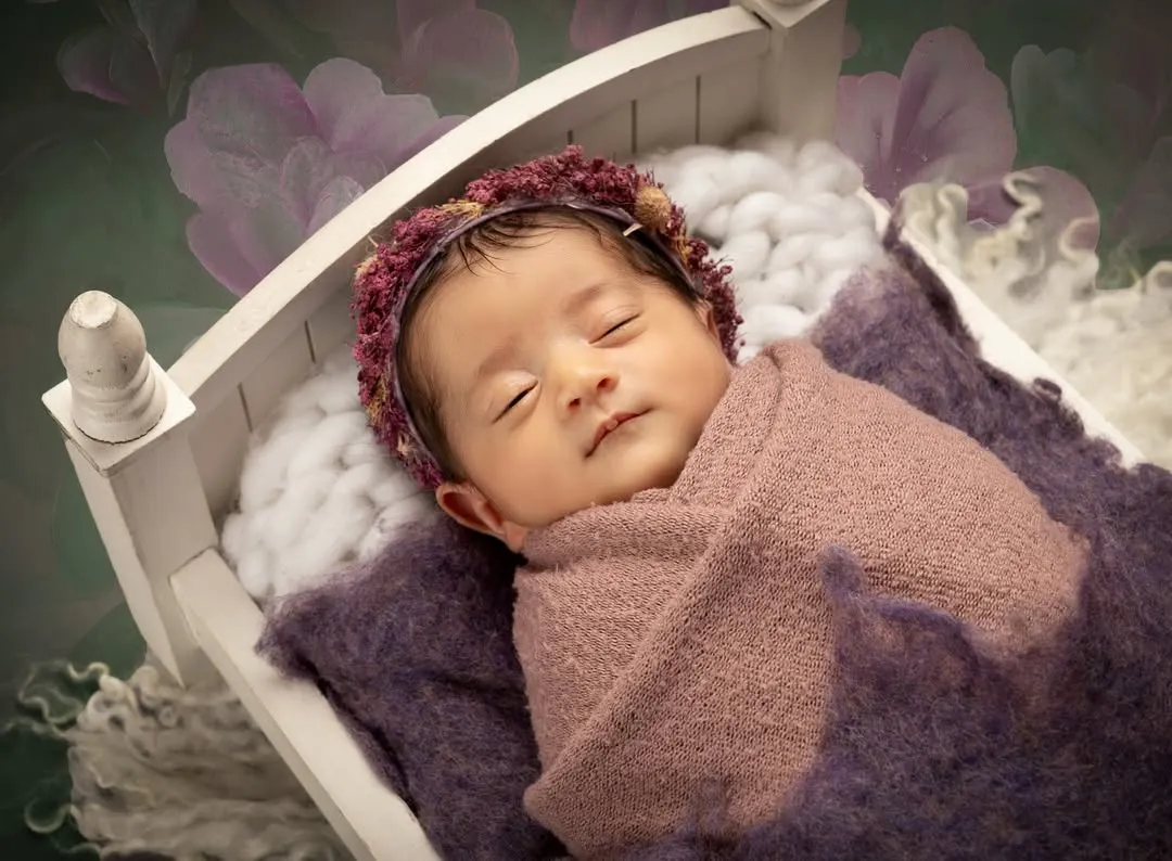 I focus on creating a safe and peaceful environment for your little one. This classic posed newborn portrait captures the serene beauty of a sleeping baby, nestled comfortably in a miniature white cot.