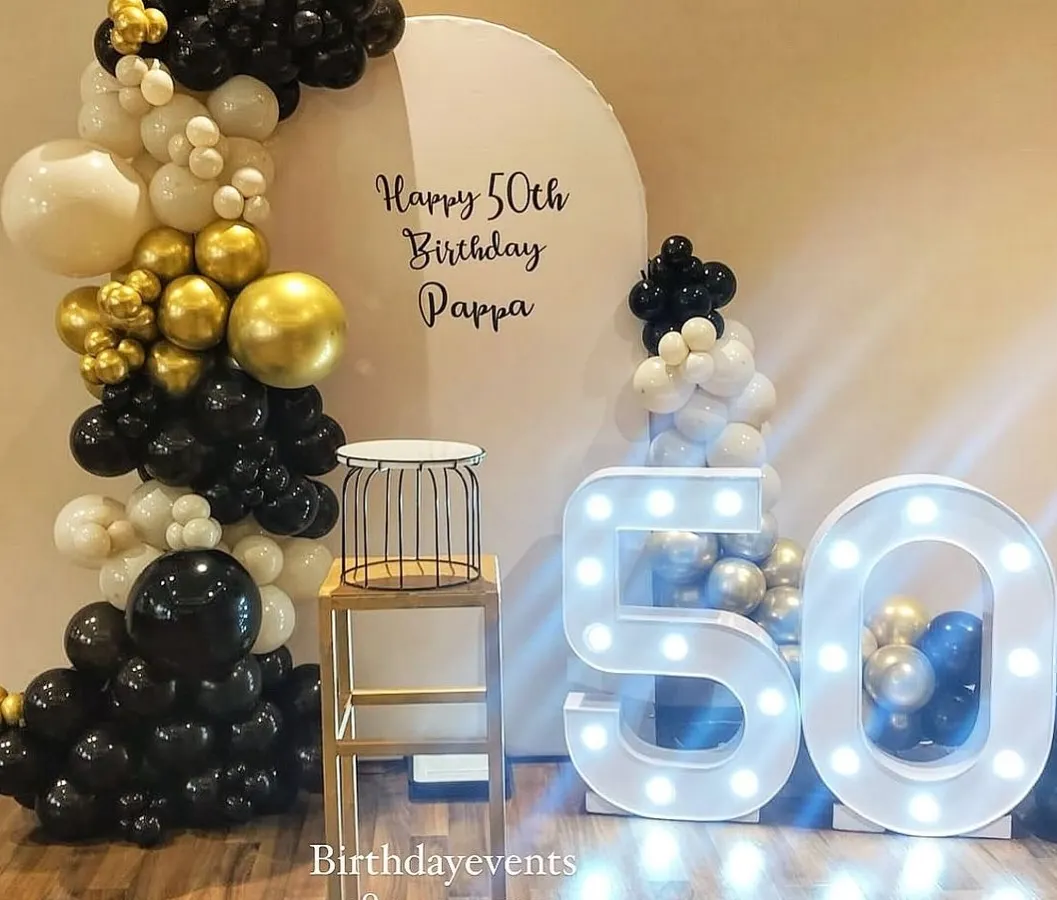 An elegant and sophisticated 50th birthday decoration for a very special celebration. The classic black, white, and gold chrome balloon arch pairs perfectly with the large marquee numbers, creating a timeless and celebratory photo corner.