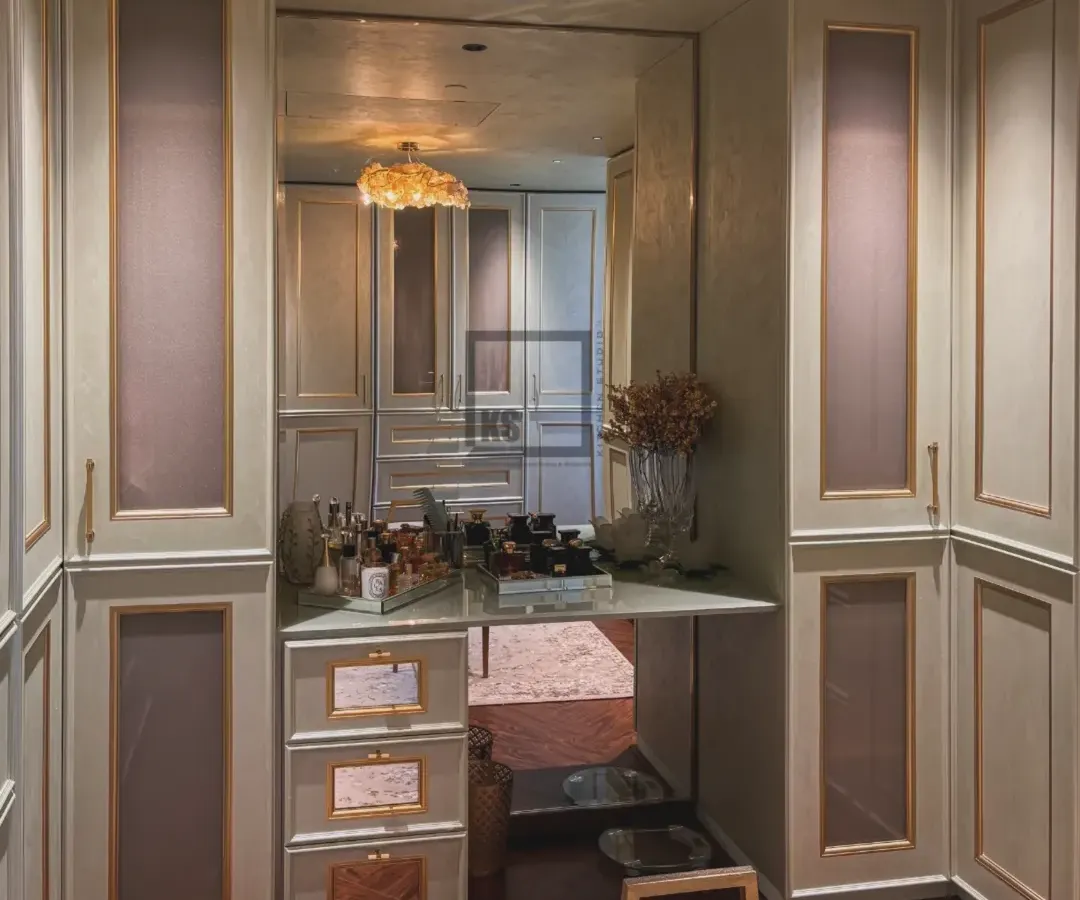 For a softer, more classic feel, this walk-in wardrobe uses gentle mint tones with elegant gold mouldings. The design includes a built-in vanity table with a large mirror, creating a bright and functional personal space.