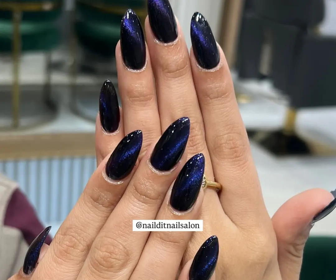 A deep galaxy effect created with magnetic cat-eye polish on long almond-shaped extensions. The dark base shifts with mesmerizing blue and purple light, offering a sleek and modern look that's perfect for any occasion.