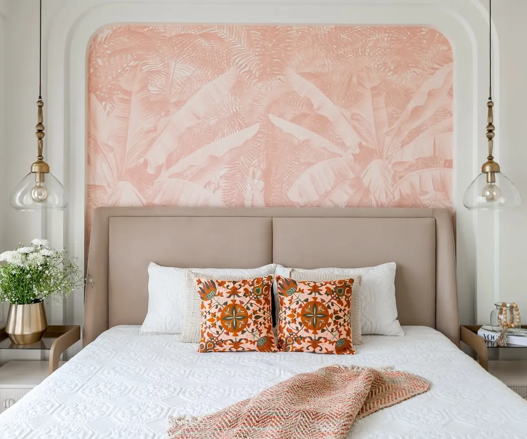 A serene master bedroom from our 'Project Lily'. We used a soft, blush-toned wallpaper with a tropical motif to create a feature wall behind the custom-upholstered bed, complemented by elegant pendant lighting for a calm and dreamy ambiance.