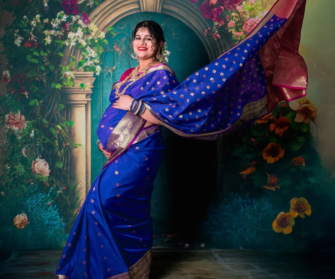 The timeless elegance of a traditional saree maternity shoot. This studio portrait uses dramatic posing and lighting to highlight the beauty of the mother-to-be and her gorgeous blue silk saree.