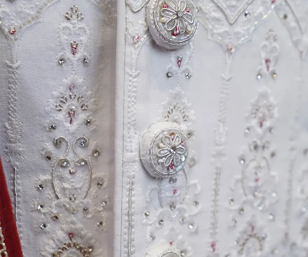 Attention to detail is everything in bespoke tailoring. This close-up shows the custom-made, fabric-covered buttons on an all-white wedding sherwani, each intricately embroidered to match the garment's delicate patterns. It’s these small touches that create a truly royal look.