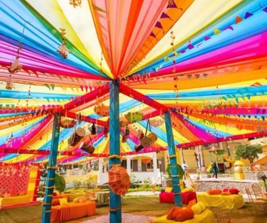 This is what a vibrant, high-energy Mehendi or Haldi ceremony looks like. The canopy of multi-colored drapes creates a festive atmosphere that is perfect for photos and celebrations.