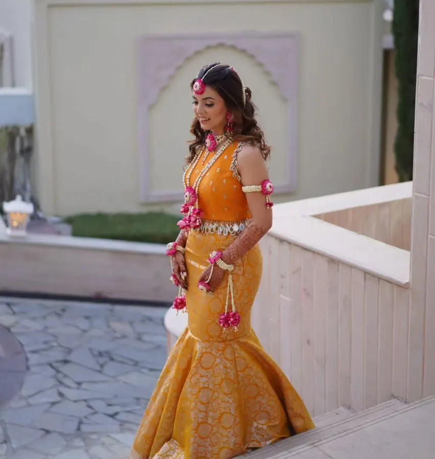 For a sunny Haldi ceremony, I designed this vibrant marigold Banarasi mermaid skirt paired with a hand-embroidered blouse. The fish-cut silhouette is a modern twist on traditional Haldi attire, and the mirror-work tassels add a playful, festive touch.