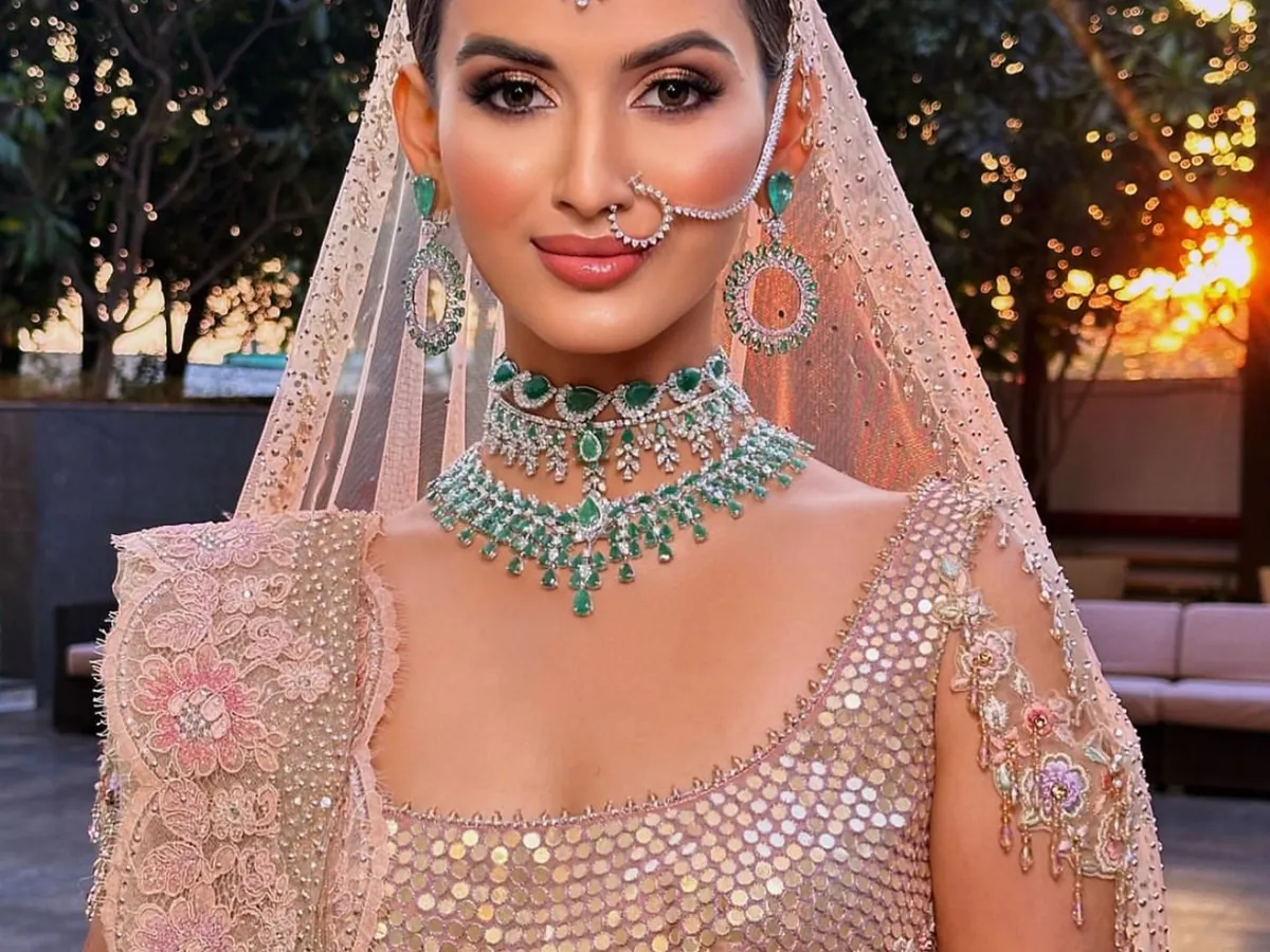 For this modern bridal look, we played with the soft light of the golden hour. The makeup features a dewy, fresh skin finish and soft pink tones on the eyes and cheeks to complement the pastel lehenga and stunning emerald jewellery.