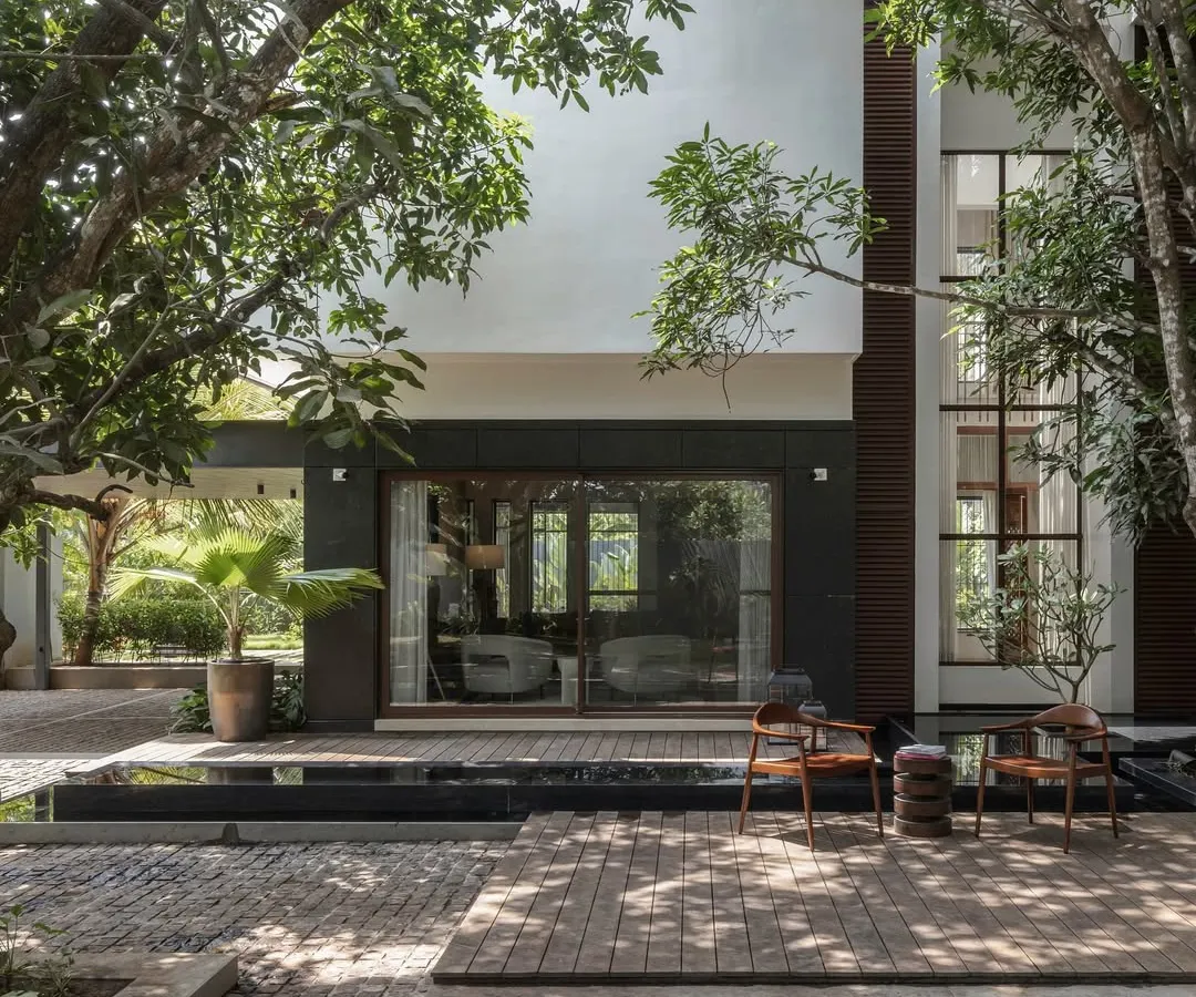 For the Mango Tree Yard residence in Kerala, we designed the home around two mature mango trees. This view from the backyard highlights the seamless blend of indoor and outdoor spaces, with a tranquil waterbody and deck creating a serene living experience connected to nature.