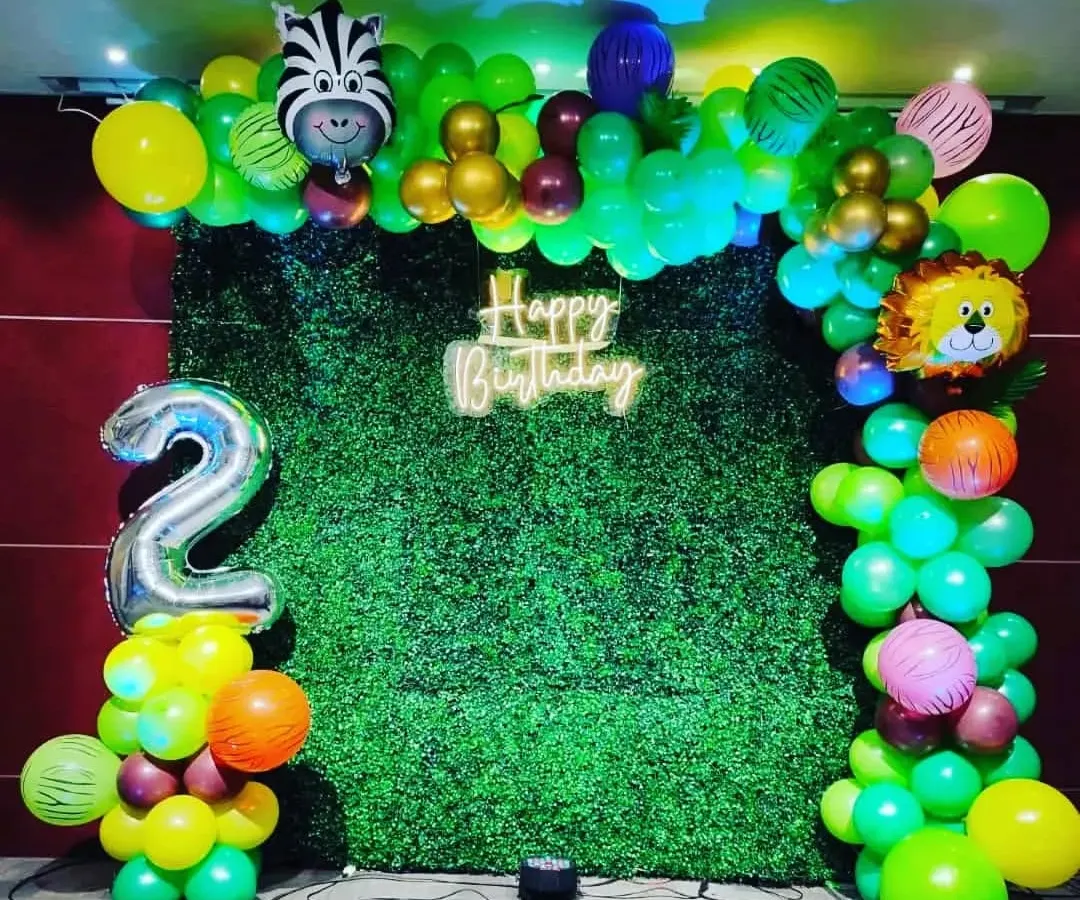 Yeh ek jungle theme birthday party ka setup hai. Isme maine grass backdrop, neon "Happy Birthday" sign, aur animal foil balloons use kiye hain. Saath mein light wala '2' number bhi hai.