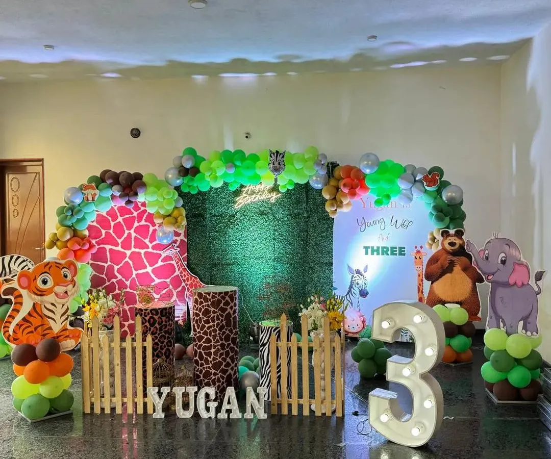 A vibrant jungle safari theme, perfect for a wild third birthday party. This setup features a lush green backdrop, fun animal cutouts like a tiger and elephant, a large light-up marquee number '3', and custom plinths with animal prints.