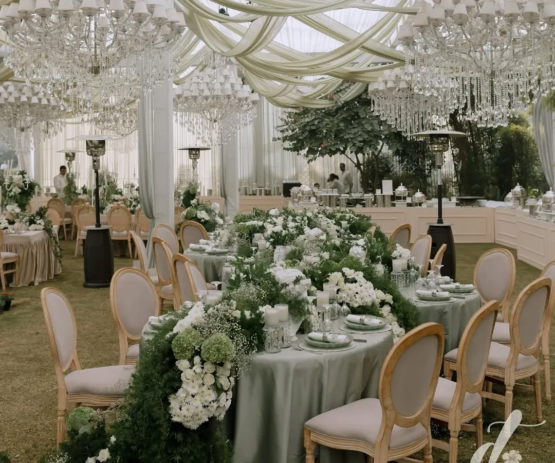 For this elegant reception, we designed a breathtaking tablescape featuring a lush floral runner cascading down the length of the table. Overhead, crystal chandeliers and soft drapery add a layer of romance and grandeur, creating a sophisticated dining experience under a custom-built marquee.