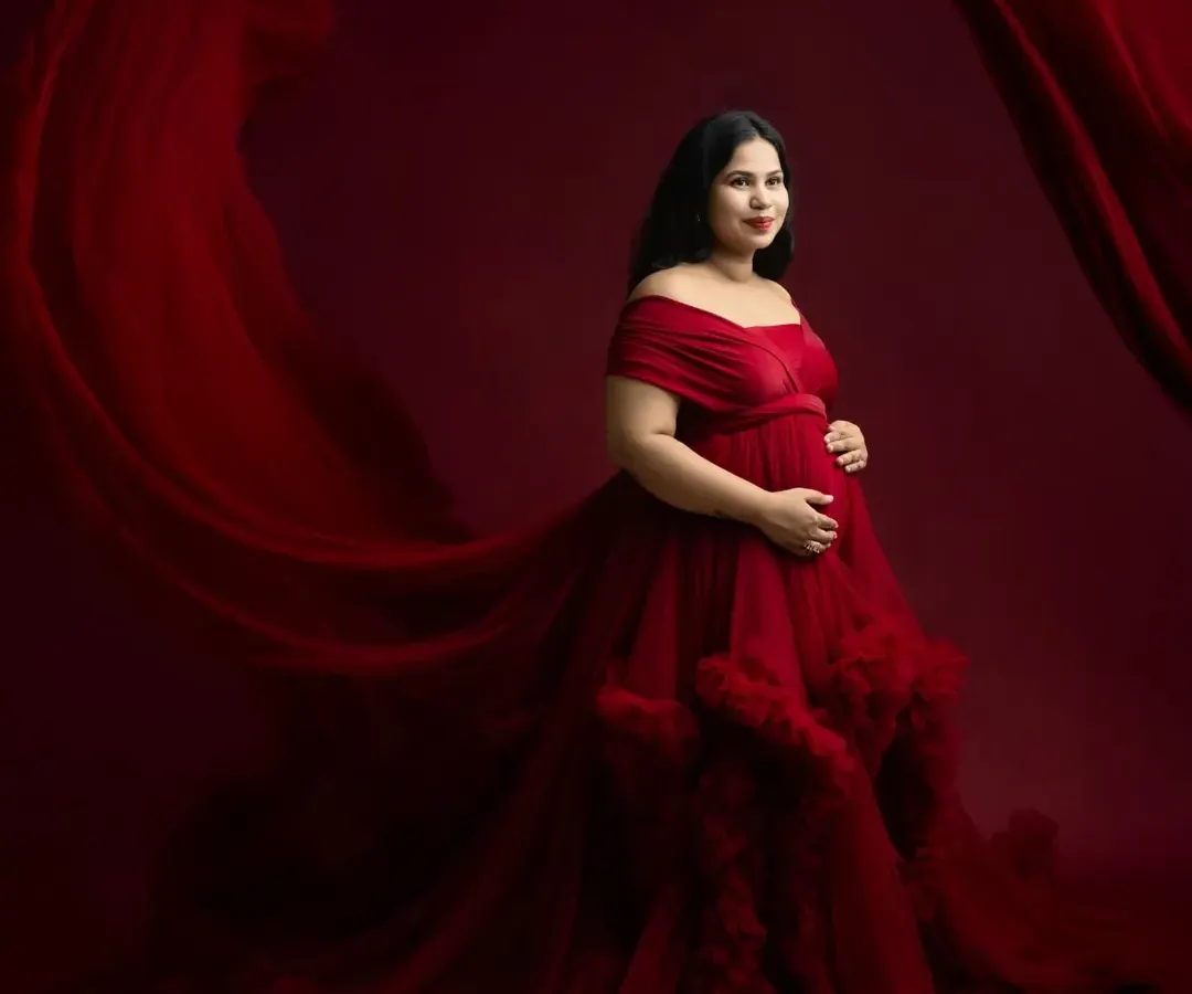 A dramatic and elegant solo maternity portrait. The flowing red gown and rich backdrop create a powerful, artistic image that celebrates the beauty of pregnancy.