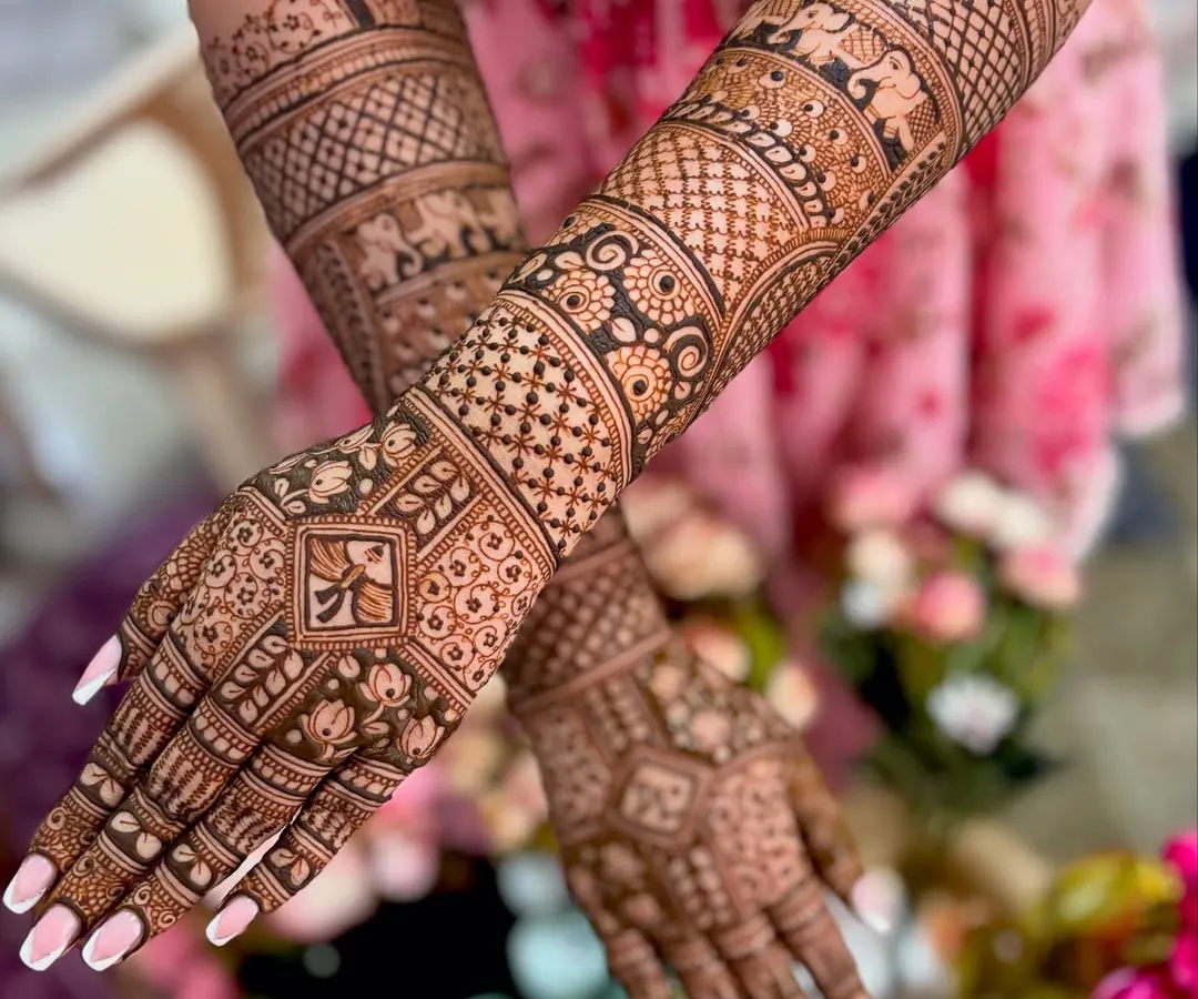 This is a classic full-coverage bridal mehendi, featuring incredibly detailed traditional patterns, including symbolic elephants and intricate geometric work extending up the forearms.