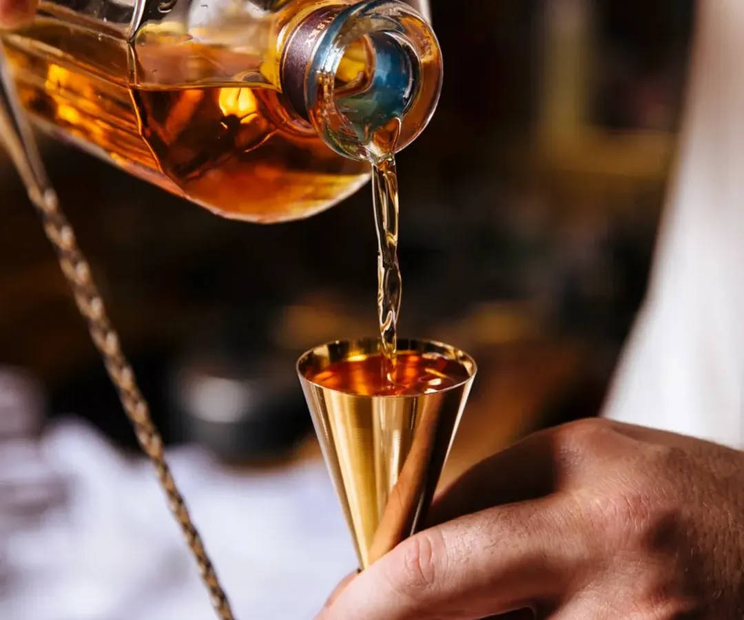 It all starts with the right technique. Here, you see the precise pour of a quality whiskey into a golden jigger, showing the professional standards I bring to every single drink we make at your event.
