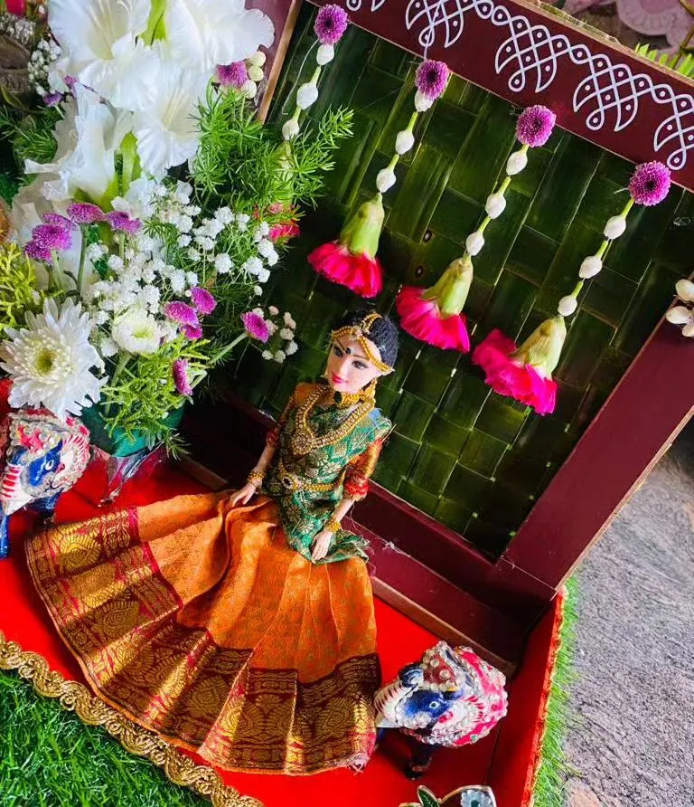 A beautiful gift platter we designed for a half saree ceremony. It features a doll dressed in a traditional orange and green saree, set against a backdrop of woven palm leaves and fresh flowers.